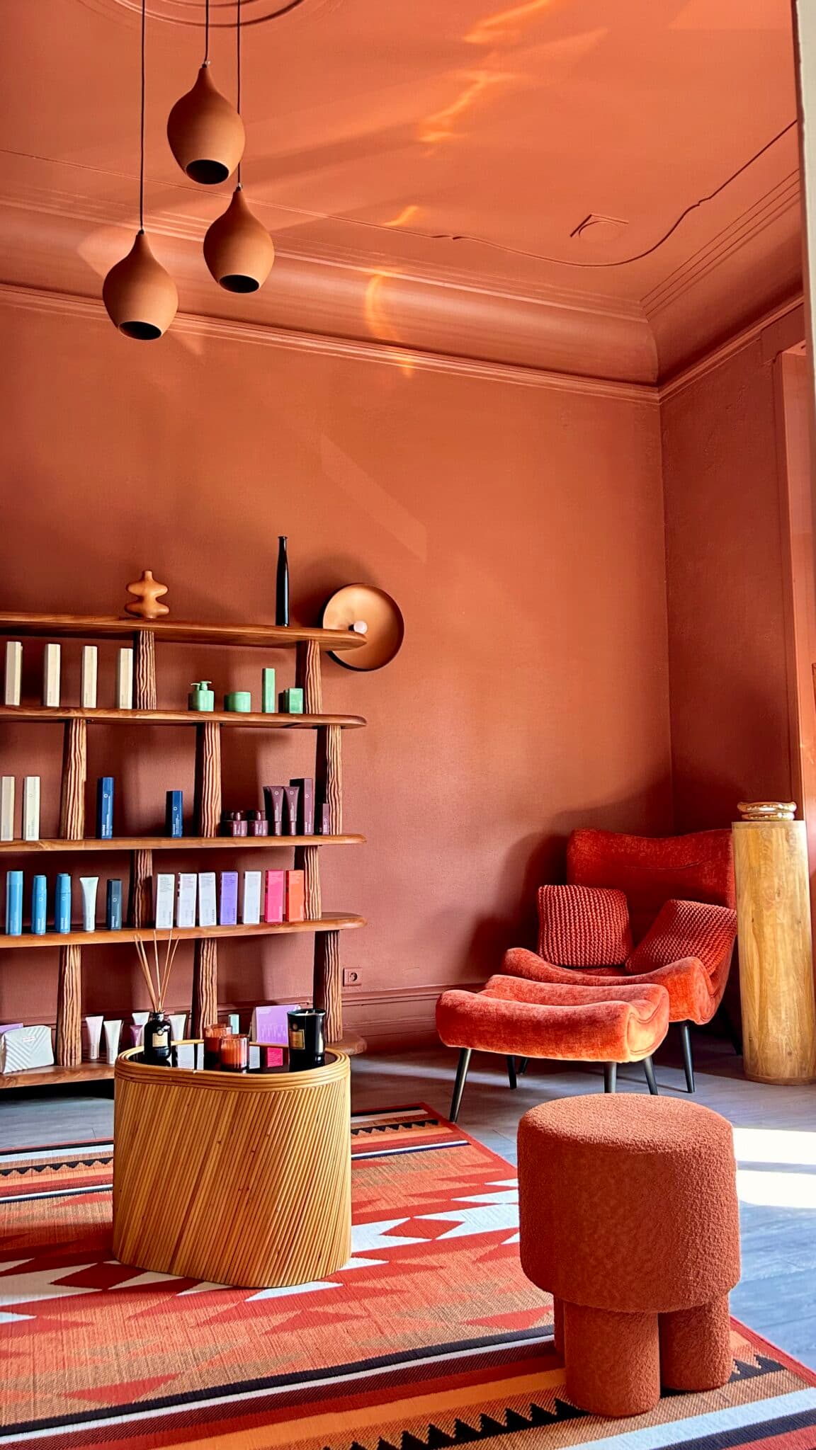 Intérieur de l'appartement Borelhahn à Thionville : fauteuil terracotta, étagères de produits, suspensions design, tapis à motifs